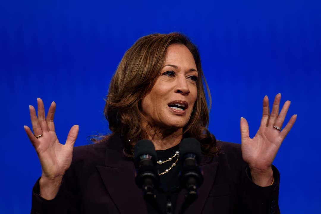 Kamala Harris speaking, holding both hands open-palmed in the air.